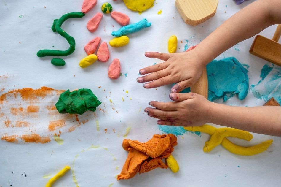 A child with only their hands showing playing with playdough