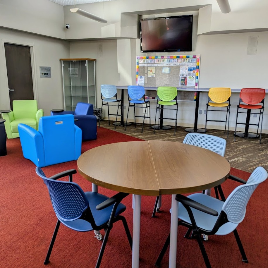 a circle table with three blue chairs surrounding it. In the background is a long bar-top table with tall rainbow-colored chairs and three small, colorful armchairs..