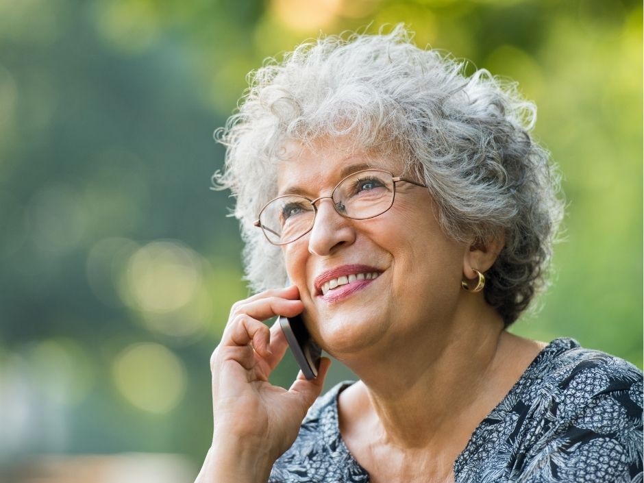 An up-close view of a senior woman with short gray hair and glasses on a cell phone